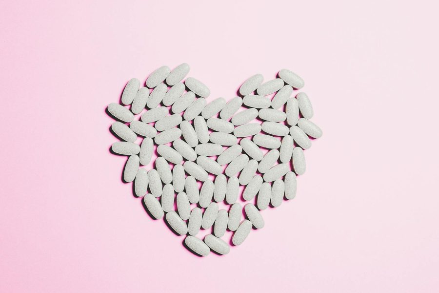 Artistic heart shape made from white pills on a pink background symbolizing love and healthcare.