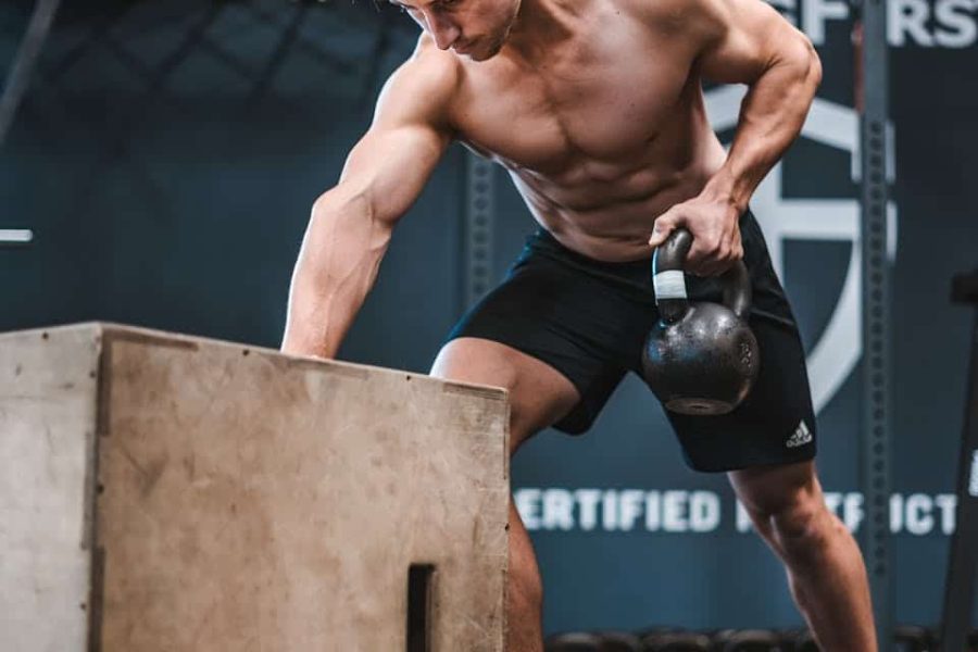 Athletic man working out with a kettlebell, showcasing strength and fitness indoors.