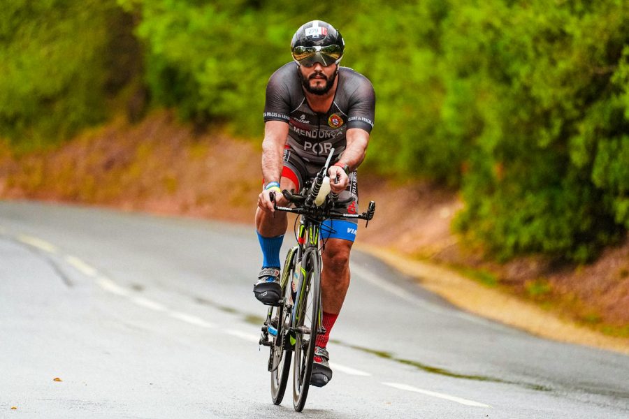 A focused cyclist racing on a road surrounded by lush greenery during summer.